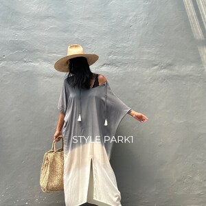 May include: A woman wearing a gray and white ombre maxi dress with a straw hat and a woven tote bag. The dress has a slit up the front and tassels on the neckline. The text "STYLE PARK1" is visible on the dress.