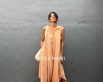 May include: A woman wearing a light brown jumpsuit with a V-neck and a white bag. The jumpsuit has a unique asymmetrical hemline and the woman is wearing gold sandals. The text "STYLE PARK1" is visible on the image.