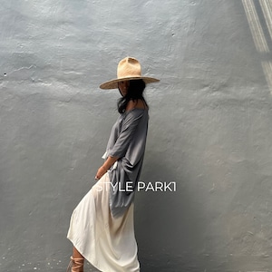 May include: A woman wearing a gray and white ombre maxi skirt, a gray oversized top, and a wide-brimmed straw hat. The text "STYLE PARKI" is visible on the skirt.