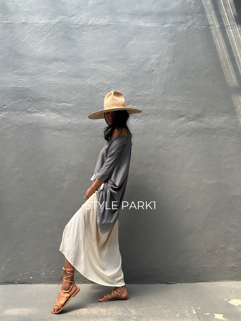 May include: A woman wearing a gray and white ombre maxi skirt, a gray oversized top, and a wide-brimmed straw hat. The text "STYLE PARKI" is visible on the skirt.