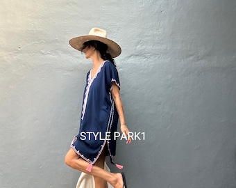 May include: A woman wearing a navy blue tunic with pink embroidery and tassels. She is wearing a wide-brimmed straw hat and black sandals. The text "STYLE PARK1" is visible on the wall behind her.