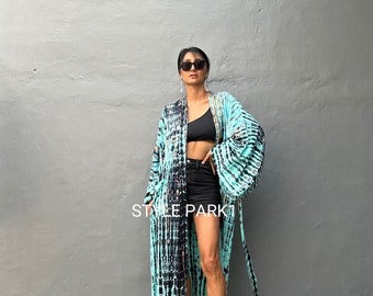 May include: A long, flowing blue and black tie-dye kimono with a gold trim. The kimono is worn over a black crop top and black denim shorts. The person is wearing gold sandals.