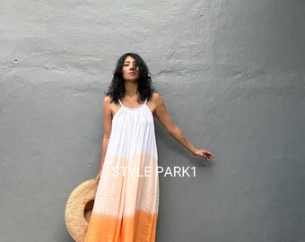 May include: A white, orange, and cream-colored maxi dress with spaghetti straps. The dress has a gradient effect, transitioning from white at the top to orange at the bottom. A straw hat is held in the left hand. The text "STYLE PARK1" is visible.