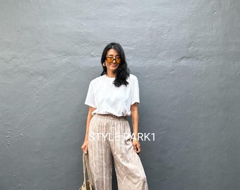 May include: A person wearing a white t-shirt and beige palazzo trousers with a leaf pattern. The person is holding a woven tote bag. The text "STYLE PARK1" is visible on the trousers.