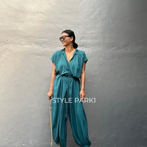Peut inclure: Une combinaison bleu sarcelle avec un col, des manches courtes et une taille &agrave; cordon de serrage. Le v&ecirc;tement pr&eacute;sente des jambes larges et fusel&eacute;es avec des poignets &eacute;lastiqu&eacute;s aux chevilles. Le texte "STYLE PARK1" est imprim&eacute; en blanc.