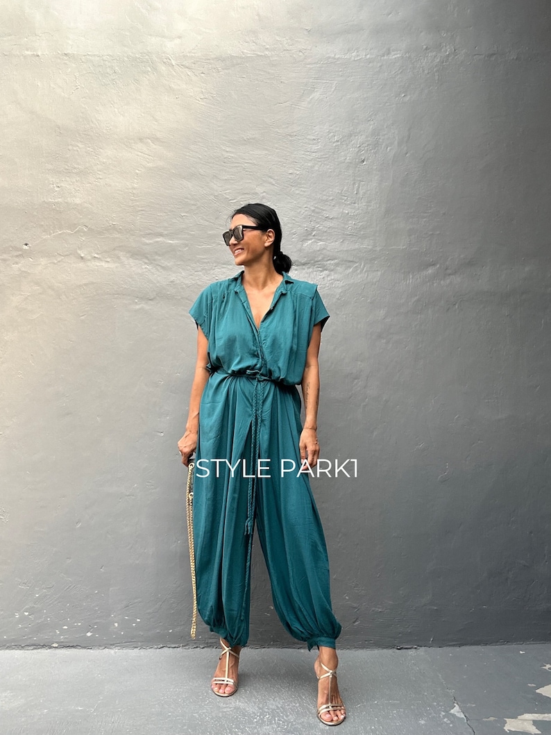 Peut inclure: Une combinaison bleu sarcelle avec un col, des manches courtes et une taille &agrave; cordon de serrage. Le v&ecirc;tement pr&eacute;sente des jambes larges et fusel&eacute;es avec des poignets &eacute;lastiqu&eacute;s aux chevilles. Le texte "STYLE PARK1" est imprim&eacute; en blanc.