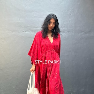 May include: A long, flowing red dress with a V-neck and a drawstring waist. The dress has a subtle pattern and is worn with a white tote bag. The text "STYLE PARK1" is visible on the dress.