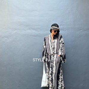 May include: A long black and white patterned dress with a matching headband. The dress has long sleeves and a belt. The text "STYLE PARIS" is visible on the image. The person is wearing black sunglasses and black heels.