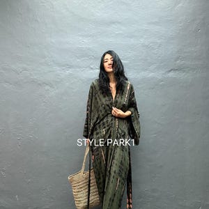 May include: A tie-dye print jumpsuit in shades of olive green and black. The wide-leg jumpsuit features a V-neckline and long, flowing sleeves. A woven tote bag with a black strap is held in the hand. The text "STYLE PARK1" is visible.