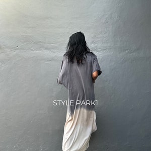 May include: A long, flowing dress with a tie-dye pattern in shades of gray and white. The dress has a loose, comfortable fit and is perfect for a casual summer look. The model is wearing gold sandals.