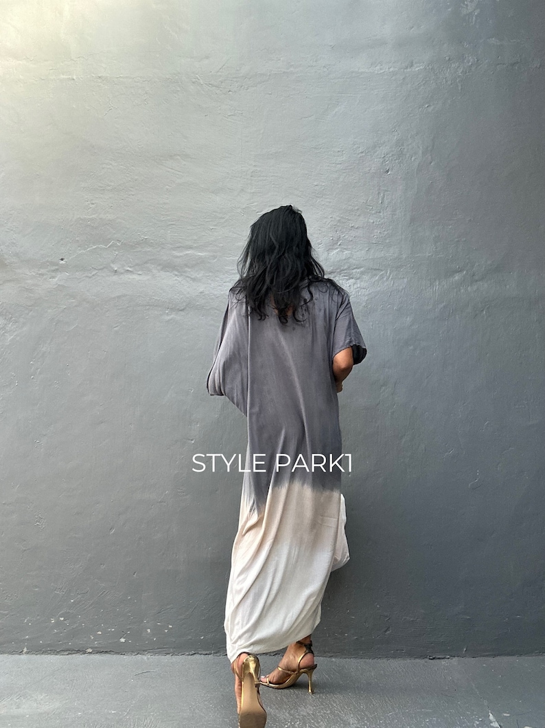 May include: A long, flowing dress with a tie-dye pattern in shades of gray and white. The dress has a loose, comfortable fit and is perfect for a casual summer look. The model is wearing gold sandals.
