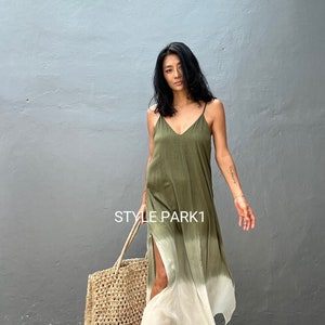 May include: A woman wearing a green and white ombre maxi dress with a side slit. She is holding a woven tote bag and is standing in front of a gray wall. The text "STYLE PARK1" is visible on the wall.