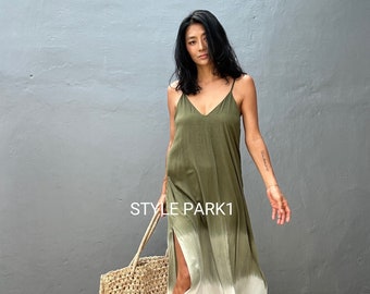 May include: A woman wearing a green and white ombre maxi dress with a side slit. She is holding a woven tote bag and is standing in front of a gray wall. The text "STYLE PARK1" is visible on the wall.