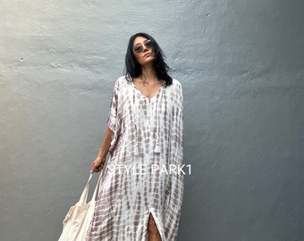 May include: A woman wearing a long, white and brown tie-dye maxi dress with a slit up the front. She is wearing sunglasses and holding a white tote bag. The text "STYLE PARK1" is visible on the dress.