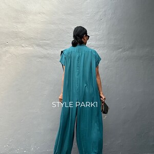 Peut inclure: Une combinaison bleu sarcelle &agrave; manches courtes, dot&eacute;e d'un col et d'une coupe ample et fluide qui se resserre au niveau des chevilles. Le v&ecirc;tement pr&eacute;sente une couture verticale centrale et le texte STYLE PARK1 imprim&eacute; en blanc au dos.