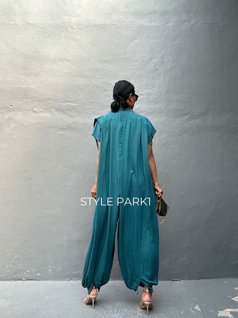 Peut inclure: Une combinaison bleu sarcelle &agrave; manches courtes, dot&eacute;e d'un col et d'une coupe ample et fluide qui se resserre au niveau des chevilles. Le v&ecirc;tement pr&eacute;sente une couture verticale centrale et le texte STYLE PARK1 imprim&eacute; en blanc au dos.
