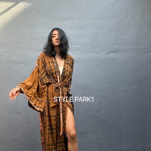 Może przedstawiać: Długa, zwiewna, brązowo-czarna szata w stylu kimono z efektem tie-dye i rozcięciem na udzie. Szata ma szerokie rękawy i pas do wiązania. Tekst "STYLE PARK1" jest widoczny po prawej stronie szaty.