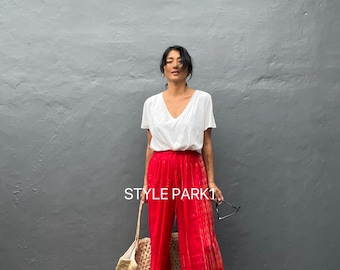 Könnte beinhalten: Eine Person trägt ein weißes V-Ausschnitt-T-Shirt und eine rote Hose mit weitem Bein und Batik-Effekt. Sie trägt eine Korbtasche und hält eine Sonnenbrille. Der Text "STYLE PARK1" ist auf der Hose zu sehen.