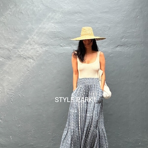 May include: A person wearing a beige vest top, wide-leg grey trousers with a white vertical stripe pattern, and a straw hat. The trousers have pockets and a ruffled hem. A white bag is over the shoulder. The text "STYLE PARKY" is visible.