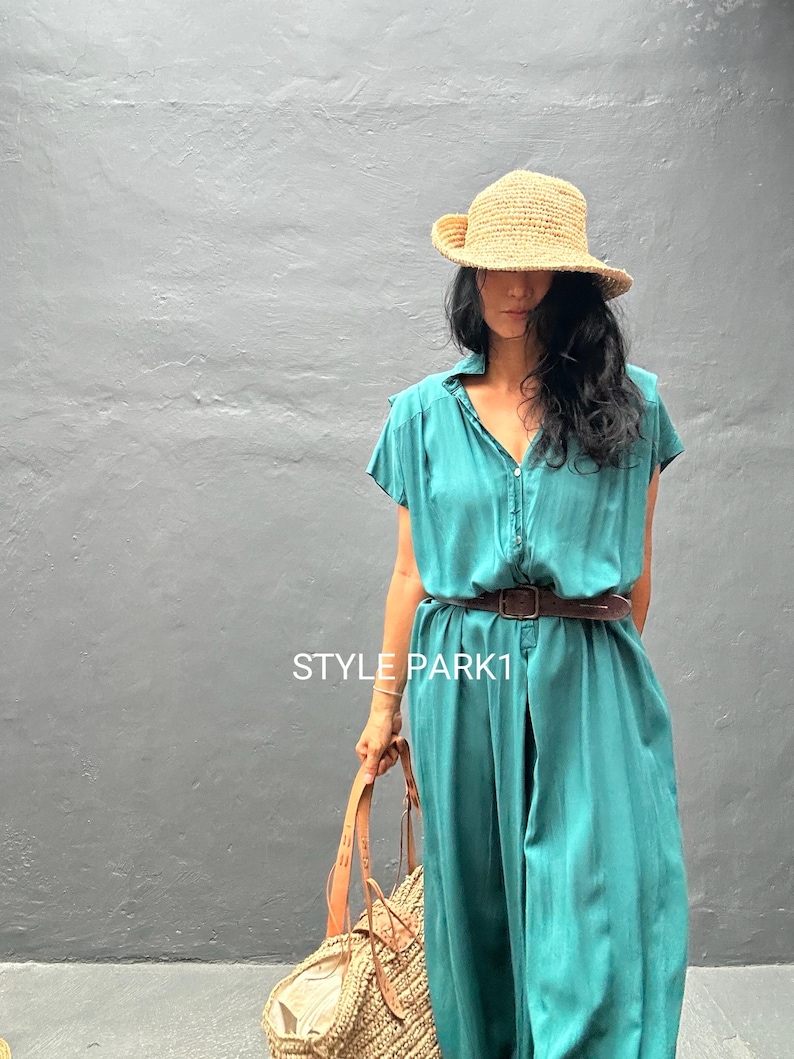 Peut inclure: Une robe boutonn&eacute;e sarcelle &agrave; manches courtes avec une ceinture en cuir marron fonc&eacute; &agrave; la taille. La robe porte le texte STYLE PARK1. Un chapeau de paille et un sac fourre-tout en paille tress&eacute;e avec des anses en cuir compl&egrave;tent l'ensemble.