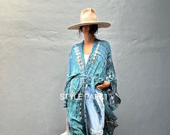 May include: A teal and black tie-dye kimono with a waist tie, worn over light blue distressed denim jeans and a white top, paired with a wide-brimmed straw hat and a white tote bag. The text STYLE PARK1 is visible on the kimono.