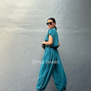 Peut inclure: Une combinaison bleu sarcelle &agrave; manches courtes, taille cintr&eacute;e et jambes fusel&eacute;es resserr&eacute;es aux chevilles. Le v&ecirc;tement pr&eacute;sente un corsage boutonn&eacute; et porte l'inscription STYLE PARK1. Le mod&egrave;le comprend un col et des poches lat&eacute;rales.