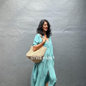 May include: A woman in a turquoise, striped maxi dress with a woven tote bag. The dress features a V-neck and a front slit. The tote bag has a leather handle and the text "STYLE PARK" is visible on the bag.