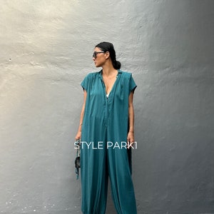 Peut inclure: Une combinaison bleu sarcelle avec un col, des manches courtes et des chevilles resserr&eacute;es. Le v&ecirc;tement pr&eacute;sente une patte de boutonnage centrale et une coupe ample. Le texte "STYLE PARK1" est imprim&eacute; en blanc au centre de la combinaison.