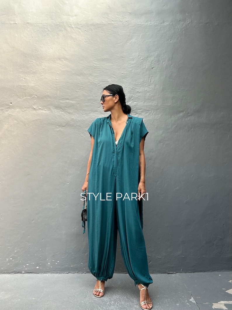 Peut inclure: Une combinaison bleu sarcelle avec un col, des manches courtes et des chevilles resserr&eacute;es. Le v&ecirc;tement pr&eacute;sente une patte de boutonnage centrale et une coupe ample. Le texte "STYLE PARK1" est imprim&eacute; en blanc au centre de la combinaison.