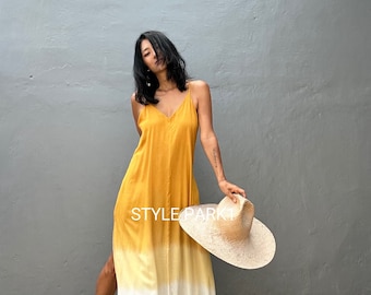 May include: A long, yellow and white ombre maxi dress with a V-neckline and a side slit. The dress is made of a lightweight fabric and has a relaxed fit. The model is wearing the dress with a straw hat and black sandals.