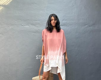 May include: A woman wearing a pink and white ombre tunic dress with a straw tote bag. The dress has a loose, flowing silhouette. The tote bag has a brown leather handle. The text "STYLE PARK1" is visible on the dress.
