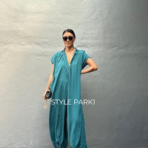 Peut inclure: Une combinaison bleu sarcelle avec un col, des manches courtes et une fermeture boutonn&eacute;e sur le devant. Le v&ecirc;tement pr&eacute;sente une coupe d&eacute;contract&eacute;e avec des ourlets fronc&eacute;s et resserr&eacute;s aux chevilles. Le texte "STYLE PARK1" est visible.
