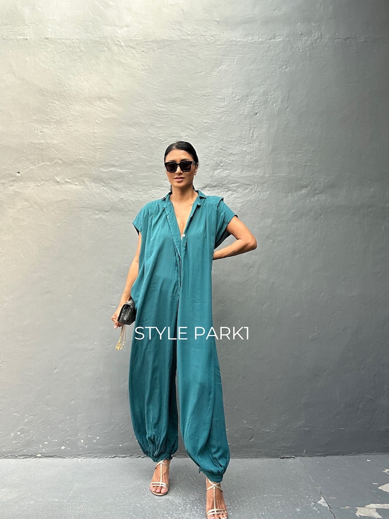 Peut inclure: Une combinaison bleu sarcelle avec un col, des manches courtes et une fermeture boutonn&eacute;e sur le devant. Le v&ecirc;tement pr&eacute;sente une coupe d&eacute;contract&eacute;e avec des ourlets fronc&eacute;s et resserr&eacute;s aux chevilles. Le texte "STYLE PARK1" est visible.