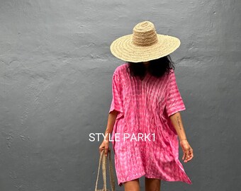 May include: A woman wearing a pink tie-dye dress, a wide-brimmed straw hat, and carrying a woven tote bag. The dress has a V-neck and short sleeves. The text "STYLE PARK1" is visible on the dress.