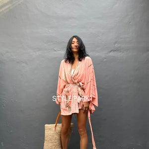 May include: A pink tie-dye kimono with a long sash. The kimono is worn by a person with long black hair. The person is standing in front of a gray wall. The text "STYLE PARK1" is visible on the kimono.