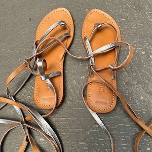 May include: A pair of brown leather sandals with silver straps and laces. The sandals are tied up the legs and have the text "Steve Madden" and "Made in Brazil" on the soles.