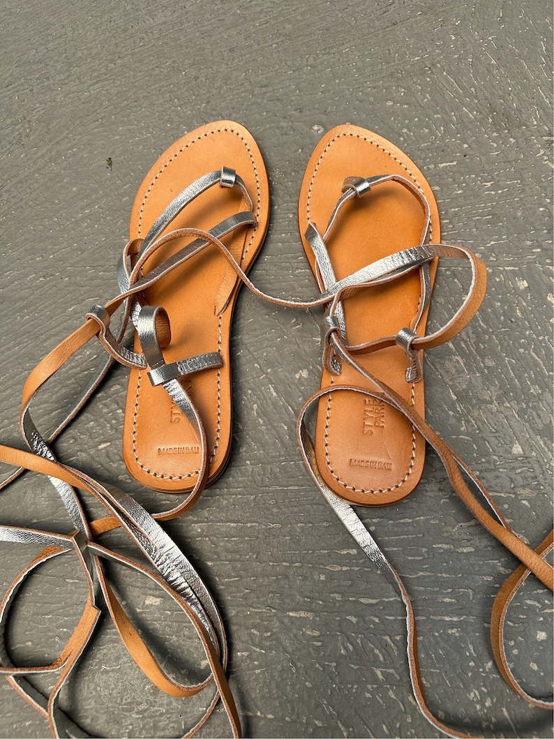 May include: A pair of brown leather sandals with silver straps and laces. The sandals are tied up the legs and have the text "Steve Madden" and "Made in Brazil" on the soles.