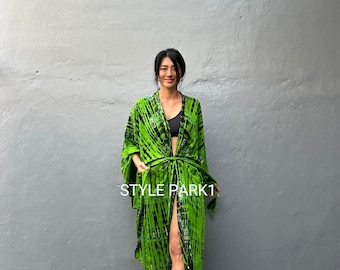 May include: A green and black tie-dye maxi dress with a long, flowing silhouette. The dress has a deep V-neckline and a tie at the waist. The model is wearing the dress with a black bra and white sandals. The text "STYLE PARK1" is visible on the dress.