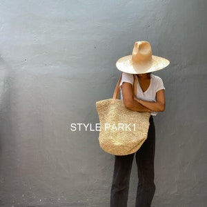 May include: A beige straw tote bag with leather handles and a wide-brimmed straw hat. The person is wearing a white t-shirt, black jeans, and silver sandals. The hat and bag are light brown. The text "STYLE PARK 1" is visible.