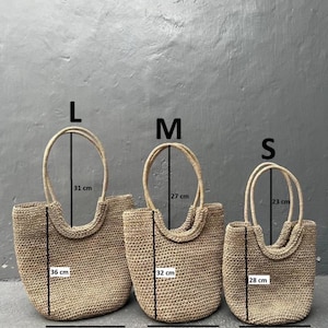 Pu&ograve; includere: Tre borse a mano in paglia di diverse dimensioni, etichettate L, M ed S. Le borse sono beige e hanno una trama intrecciata. Le misure di ogni borsa sono indicate in centimetri.