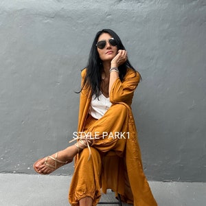 May include: A woman wearing a mustard yellow jumpsuit with a long, matching cardigan. She is wearing sunglasses and has her hair down. The text "STYLE PARK1" is visible in the image.