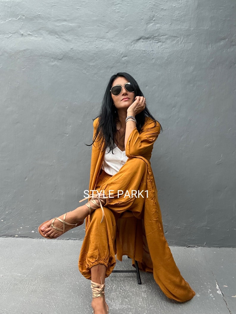 May include: A woman wearing a mustard yellow jumpsuit with a long, matching cardigan. She is wearing sunglasses and has her hair down. The text "STYLE PARK1" is visible in the image.