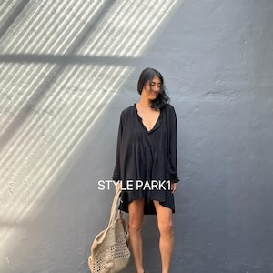 Puede incluir: Una mujer lleva un vestido negro de manga larga con cuello en V y ribete de ganchillo. Lleva un bolso tote grande de ganchillo marrón claro y sandalias de tacón negras. El texto "STYLE PARK1" es visible en la imagen.