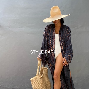May include: A woman wearing a long, flowing tie-dye kimono in navy and rust, with a wide-brimmed straw hat and a woven tote bag. The text "STYLE PARK1" is visible on the kimono.