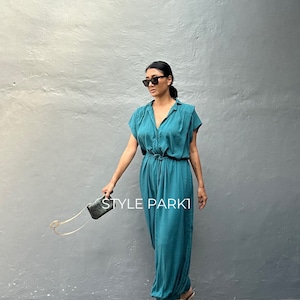 Peut inclure: Une combinaison bleu sarcelle avec un col, des manches courtes et une taille &agrave; cordon. Le v&ecirc;tement pr&eacute;sente une fermeture boutonn&eacute;e sur le devant et des jambes amples. Une petite pochette rectangulaire textur&eacute;e avec une cha&icirc;ne dor&eacute;e.