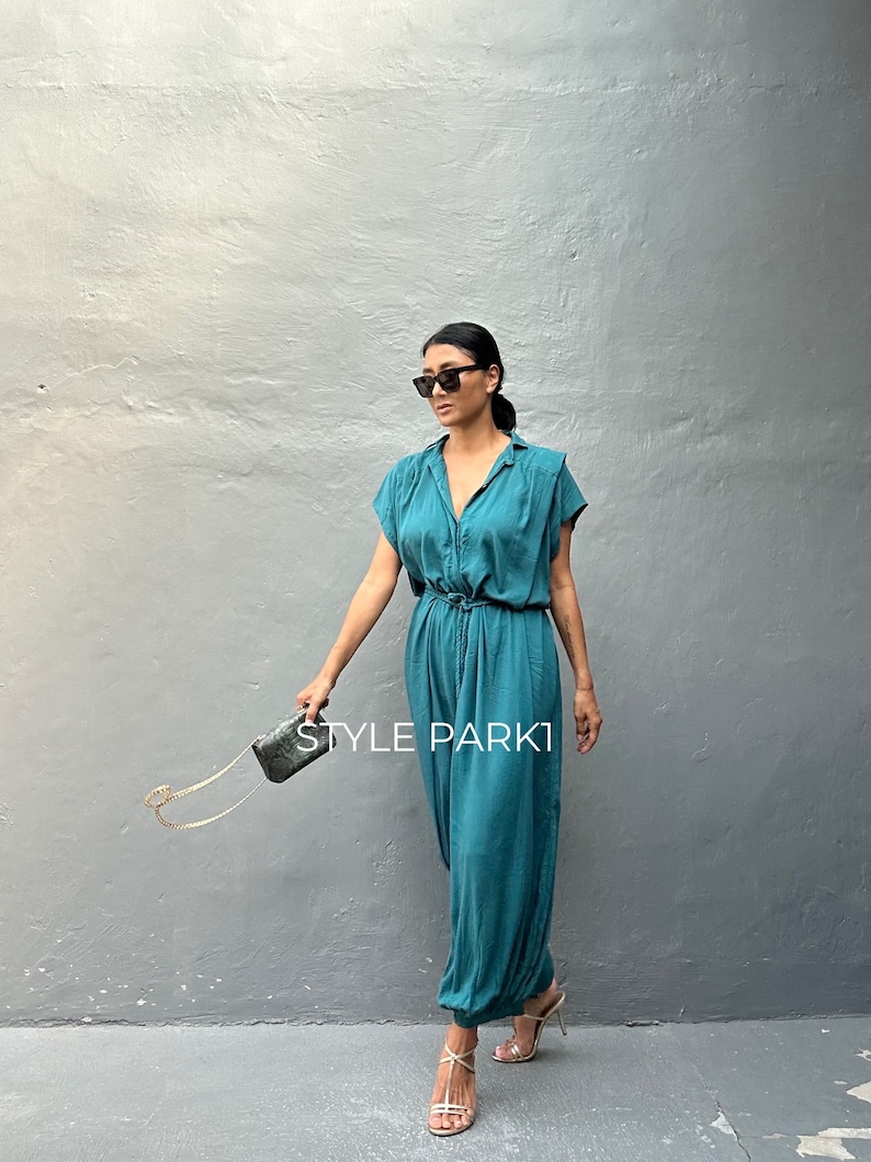 Peut inclure: Une combinaison bleu sarcelle avec un col, des manches courtes et une taille &agrave; cordon. Le v&ecirc;tement pr&eacute;sente une fermeture boutonn&eacute;e sur le devant et des jambes amples. Une petite pochette rectangulaire textur&eacute;e avec une cha&icirc;ne dor&eacute;e.