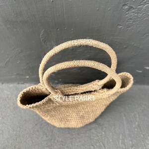 Pu&ograve; includere: Una borsa tote in tessuto marrone chiaro con doppie maniglie. La borsa ha una forma leggermente arrotondata ed &egrave; realizzata in materiale naturale. Il testo "STYLE PARK1" &egrave; visibile sulla borsa.