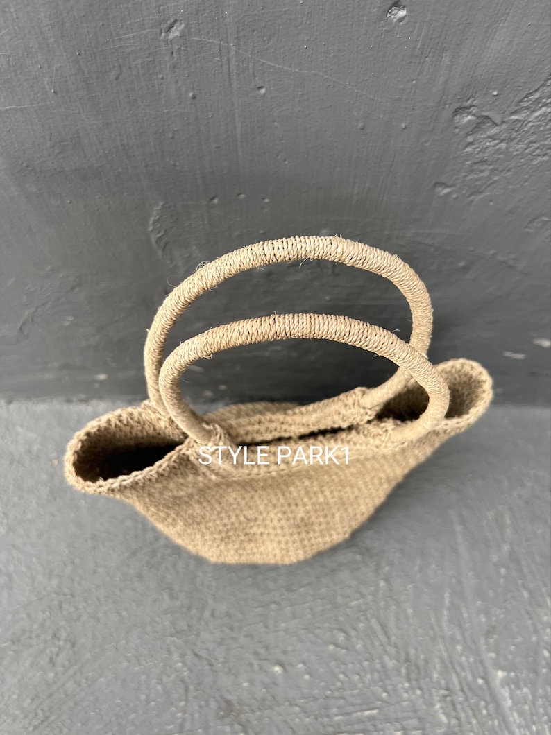 Pu&ograve; includere: Una borsa tote in tessuto marrone chiaro con doppie maniglie. La borsa ha una forma leggermente arrotondata ed &egrave; realizzata in materiale naturale. Il testo "STYLE PARK1" &egrave; visibile sulla borsa.