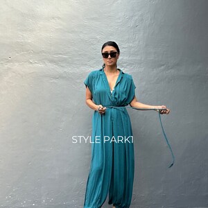 Peut inclure: Une combinaison bleu sarcelle &agrave; manches courtes, dot&eacute;e d'un d&eacute;collet&eacute; en V et d'une fine ceinture &agrave; nouer assortie &agrave; la taille. Le v&ecirc;tement pr&eacute;sente une coupe d&eacute;contract&eacute;e avec des jambes fusel&eacute;es et le texte STYLE PARK1 imprim&eacute; en blanc.