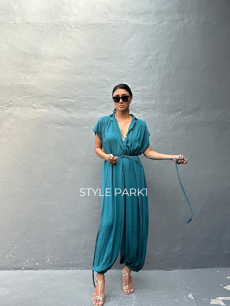 Peut inclure: Une combinaison bleu sarcelle &agrave; manches courtes, dot&eacute;e d'un d&eacute;collet&eacute; en V et d'une fine ceinture &agrave; nouer assortie &agrave; la taille. Le v&ecirc;tement pr&eacute;sente une coupe d&eacute;contract&eacute;e avec des jambes fusel&eacute;es et le texte STYLE PARK1 imprim&eacute; en blanc.